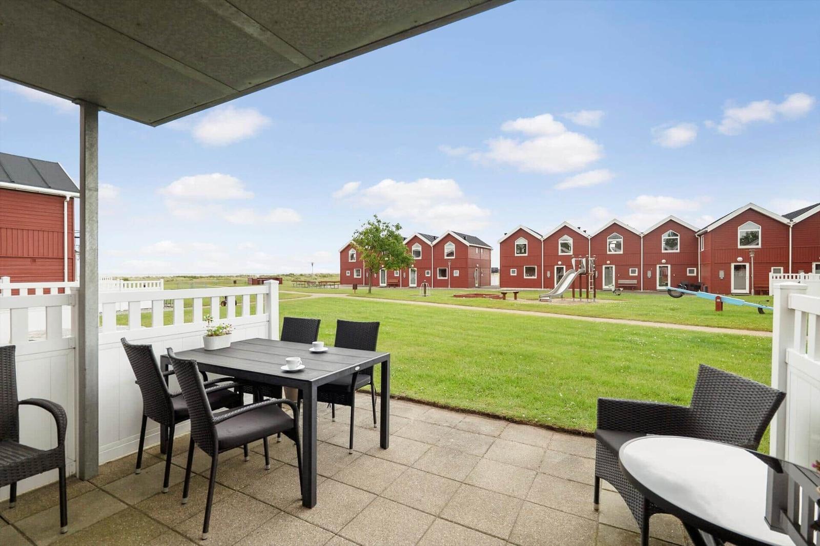 Terrasse mit Tisch und Stühlen. Blick auf rote Häuser und Grünfläche mit Spielplatz.