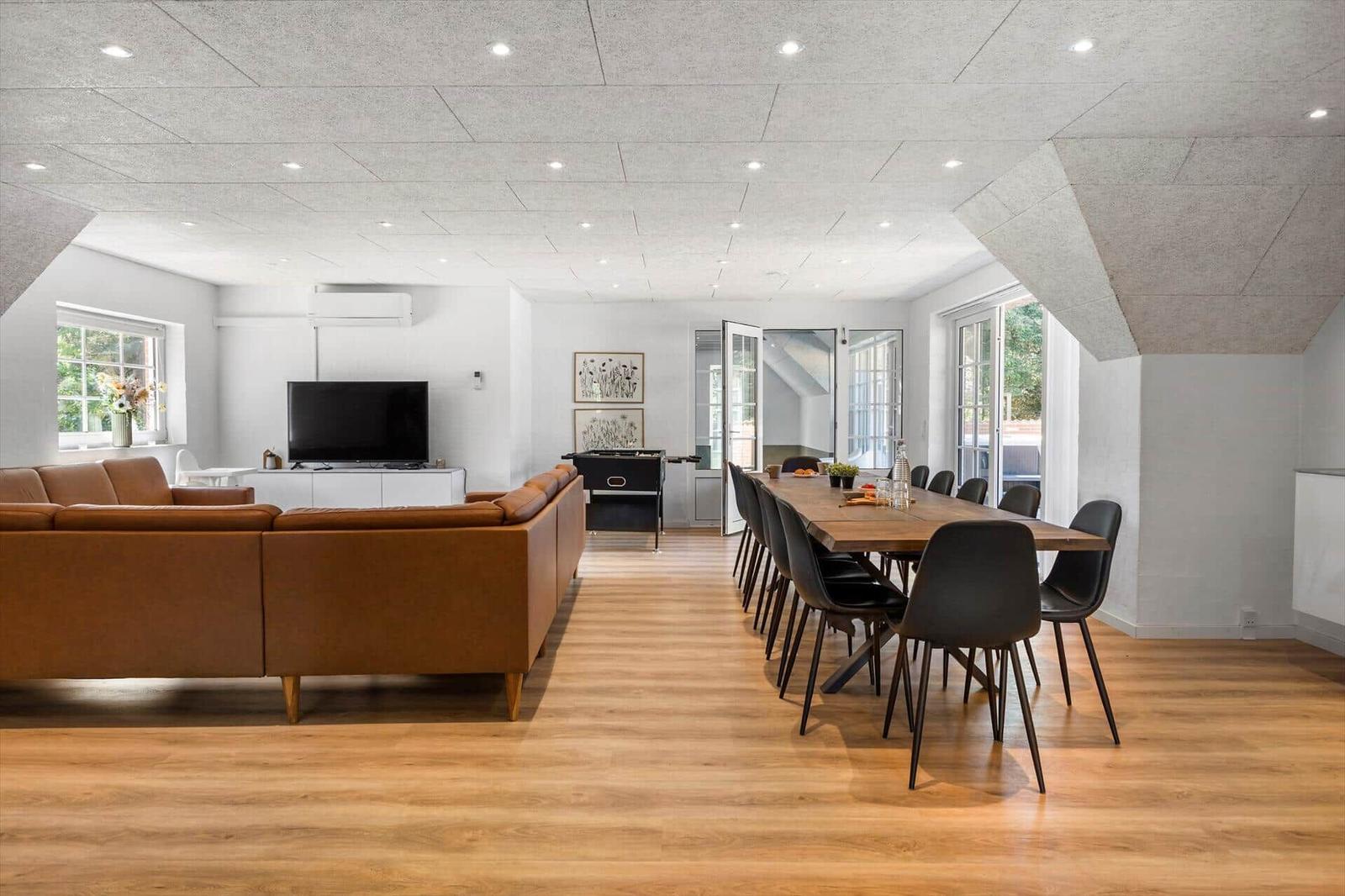 Großes Wohn- und Esszimmer mit braunem Sofa, Holzboden und langem Esstisch mit Stühlen.