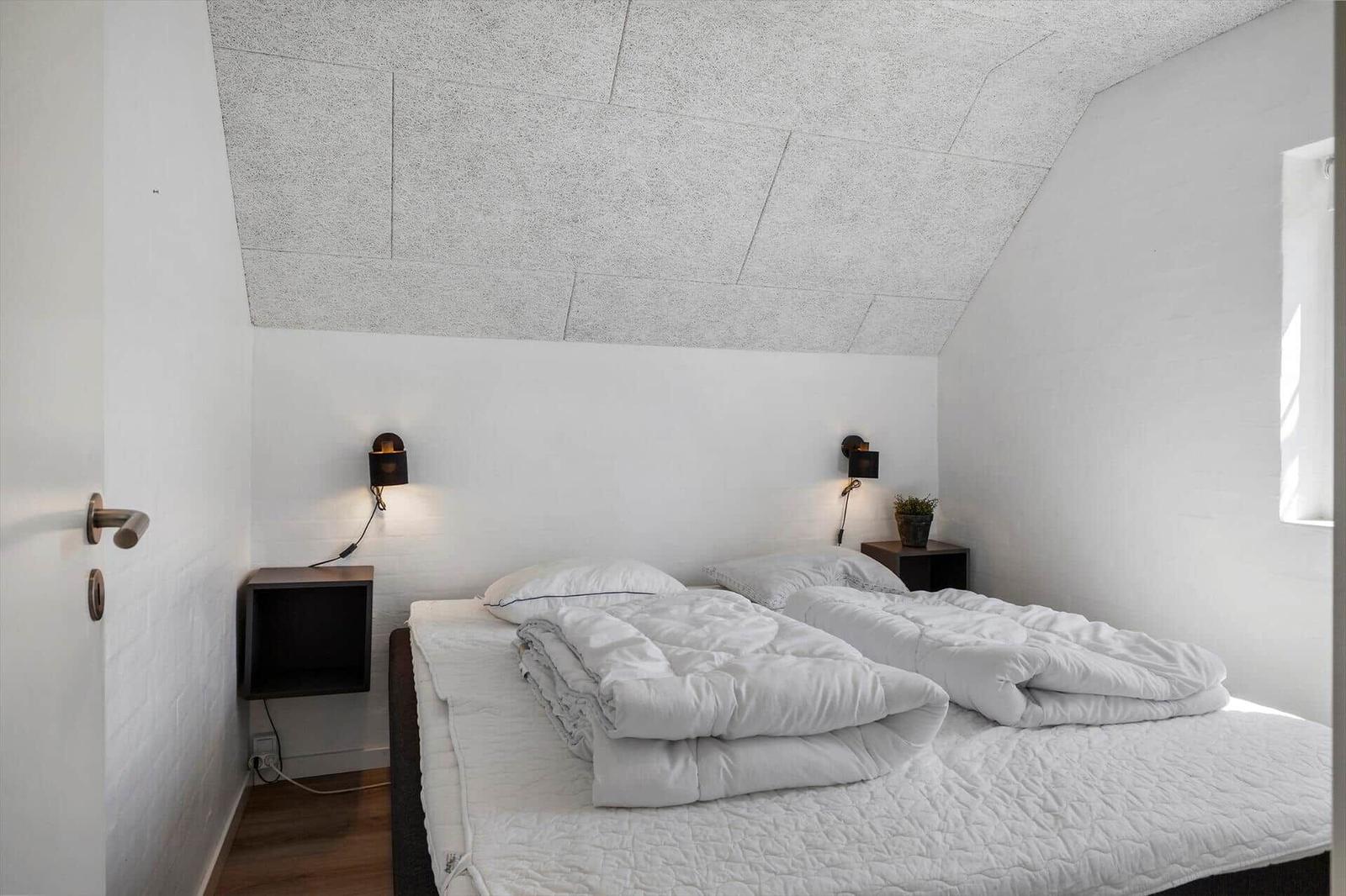 Schlafzimmer mit Doppelbett, weißen Wänden und schrägen Deckenpaneelen.