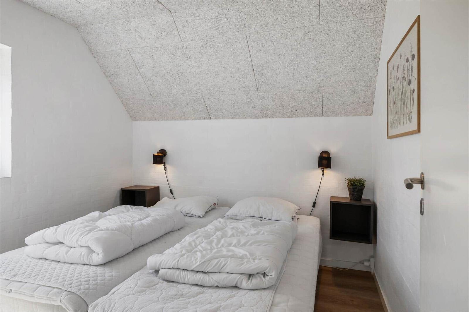 Schlafzimmer mit zwei Betten, weißen Wänden und schrägem Dach