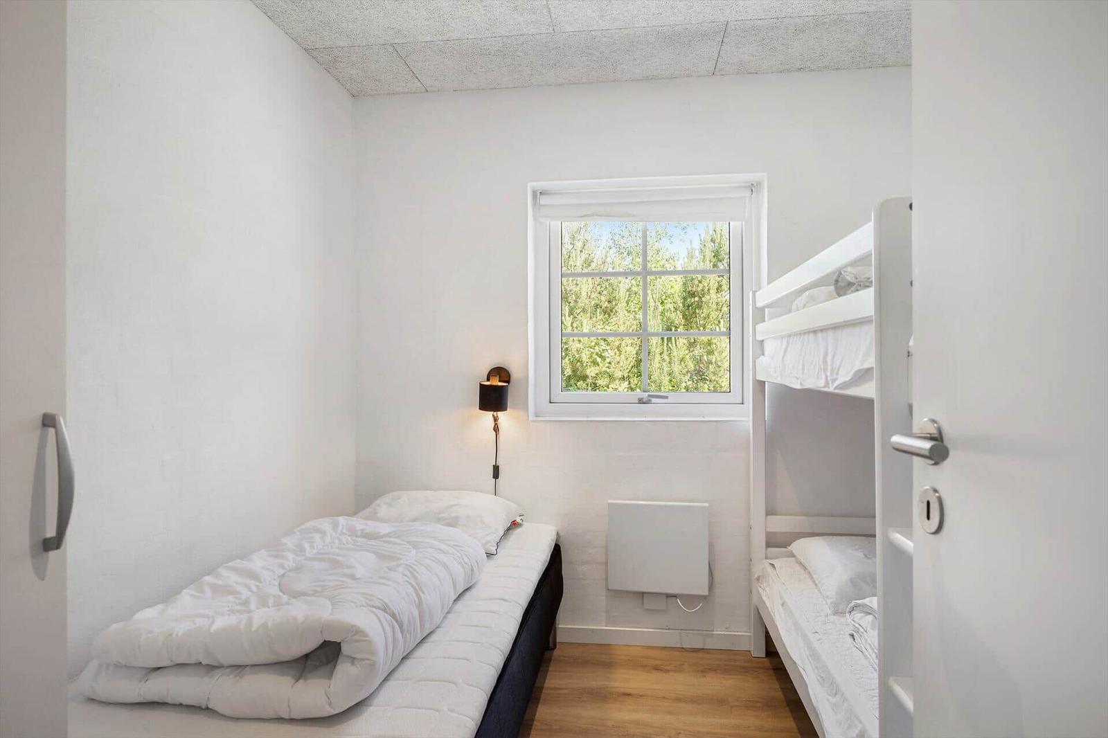 Zimmer mit Einzelbett und Doppelstockbett, Fenster mit Blick auf Grün.