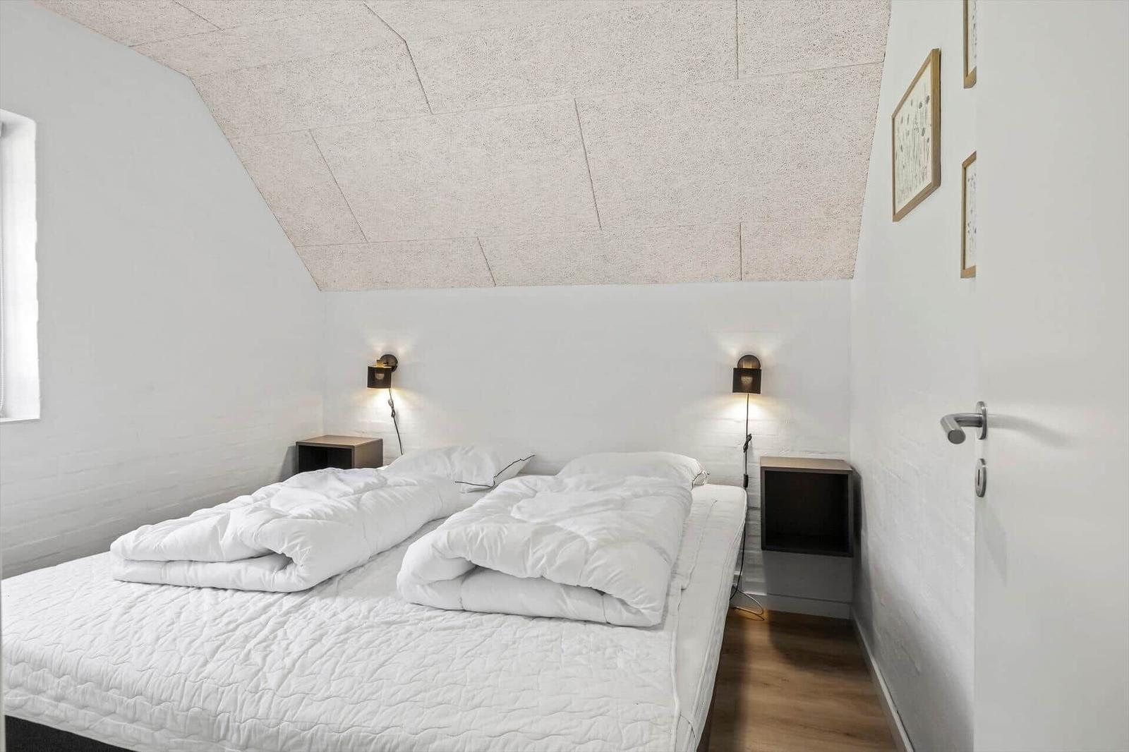 Schlafzimmer mit Doppelbett, zwei Nachttischen und einer schrägen Decke.