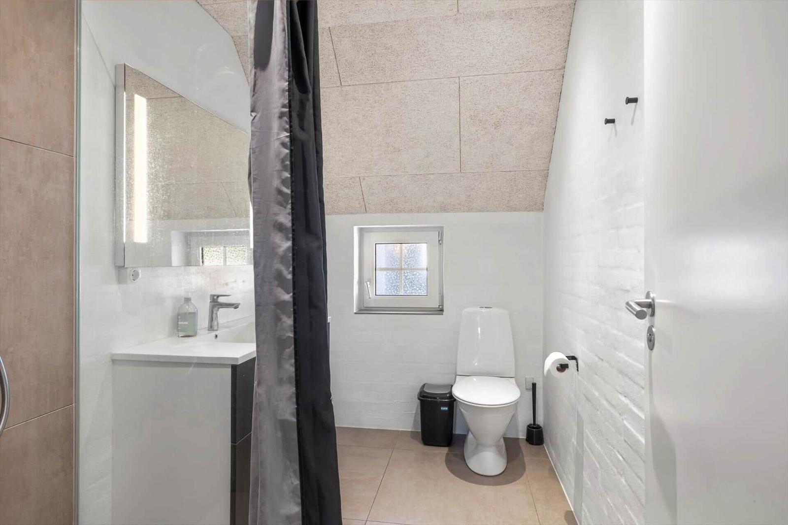 Badezimmer mit Toilette, Waschbecken und Dusche. Fenster mit Glassteinen.