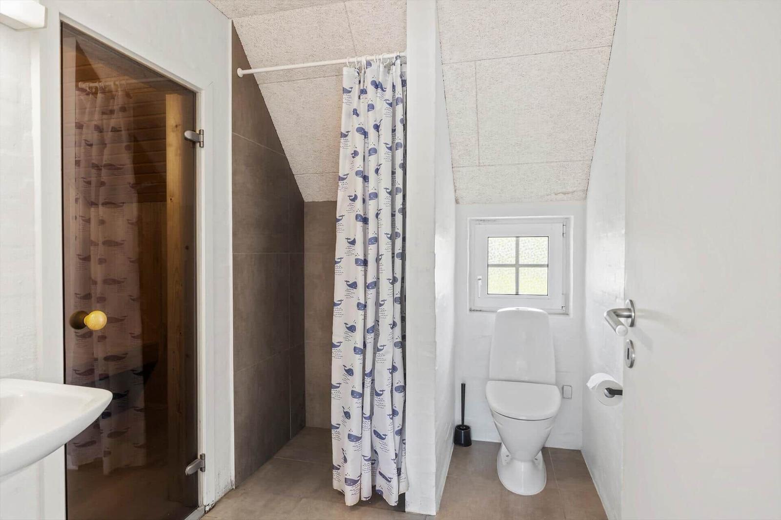 Badezimmer mit Dusche, Toilette und Fenster. Duschvorhang mit Walenmotiv.