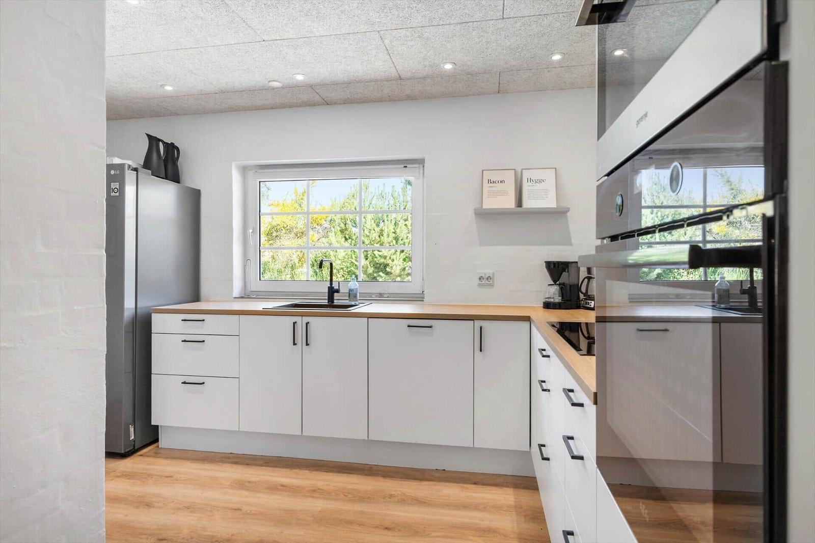 Moderne Küche mit weißer Einbauküche, Holzoberflächen und Fensterblick auf Grün.