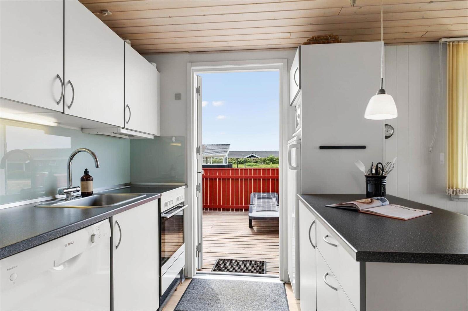 Küche mit Blick auf Balkon mit rotem Geländer und Liegestuhl.