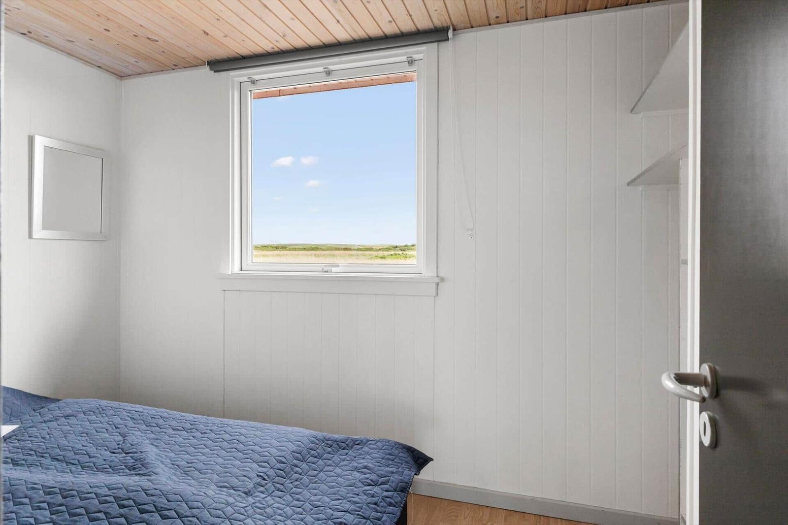 Schlafzimmer mit Bett, Fenster und Kleiderschrank. Blick auf Feld.