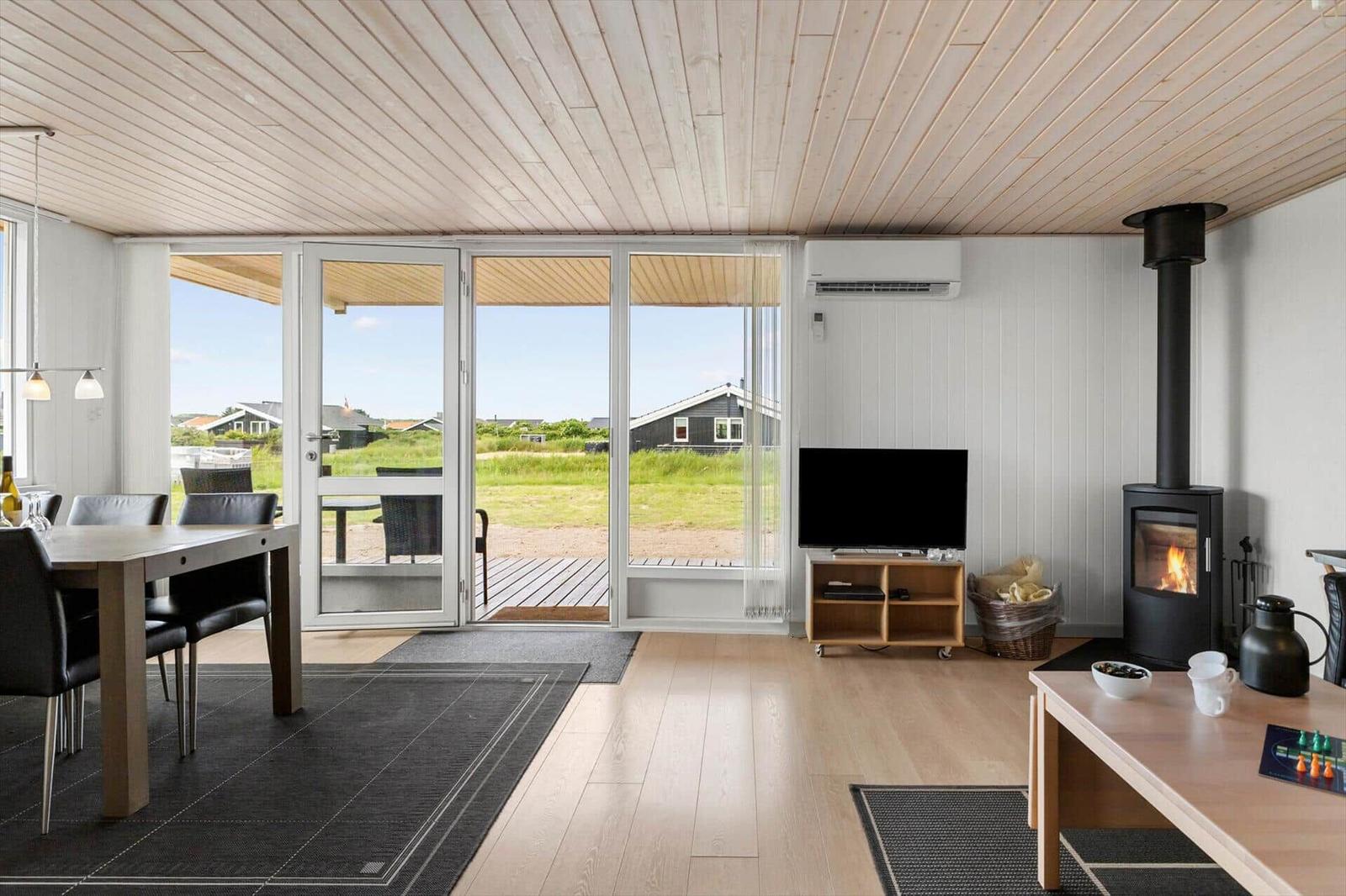Wohn- und Essbereich mit Holzboden, TV, Kaminofen und Terrasse mit Blick auf Grasland.