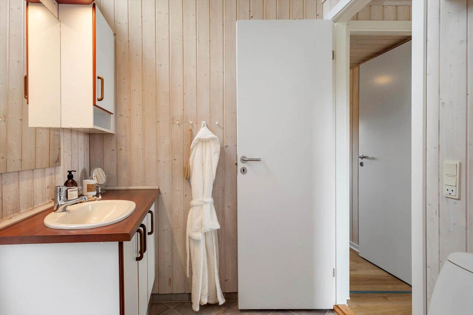 Badezimmer mit Waschbecken, Spiegelschrank und Bademantel an der Wand.
