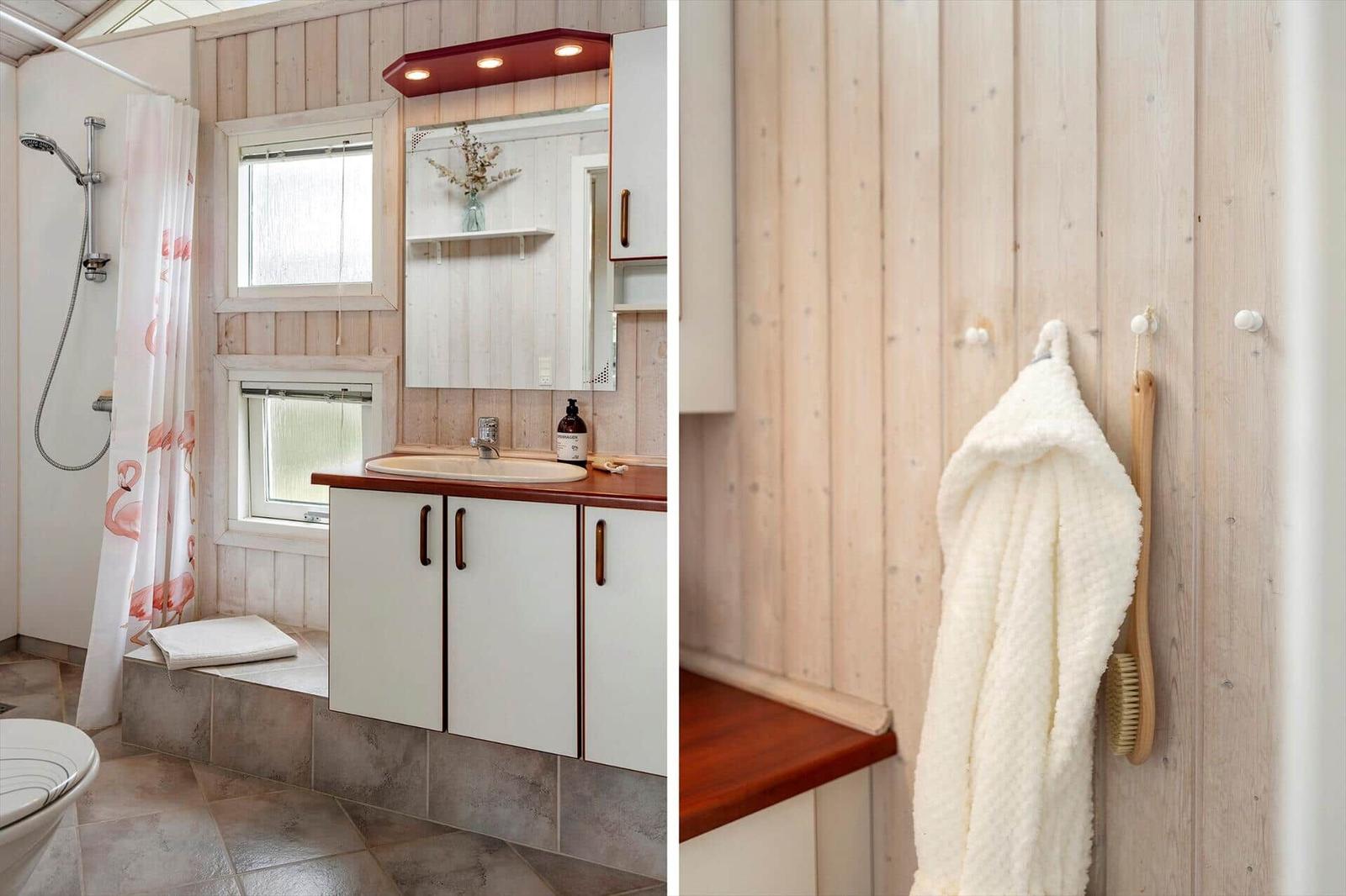 Badezimmer mit Dusche, Waschbecken und Holzwand. Handtuch und Bürste hängen an Haken.