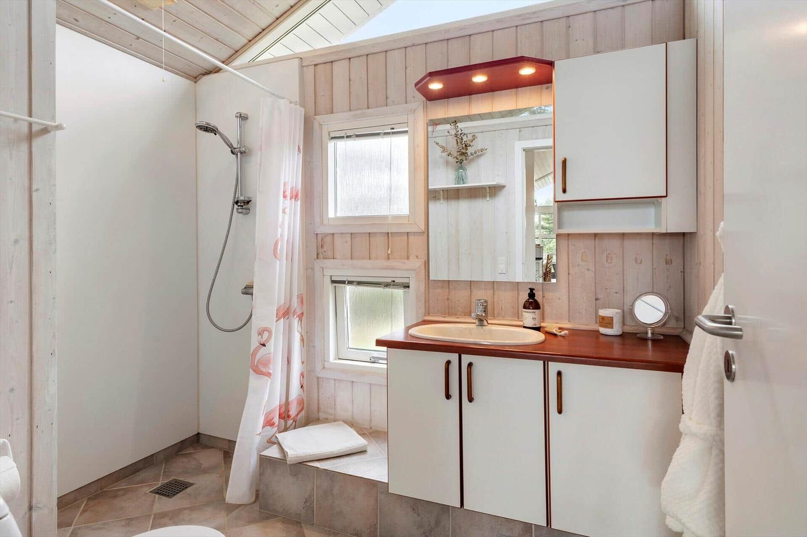 Badezimmer mit Dusche, Waschbecken und Spiegelschrank. Holzwand und Dachfenster.