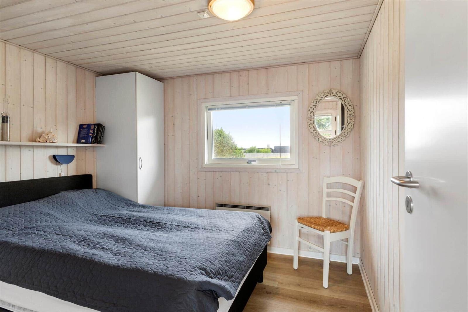 Schlafzimmer mit Bett, Schrank, Stuhl und Fenster.