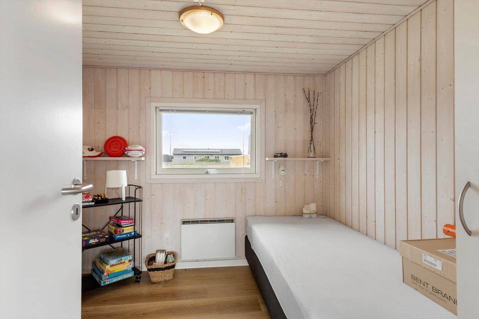 Ein Schlafzimmer mit Holzwand, Bett, Fenster und Regal mit Spielen.