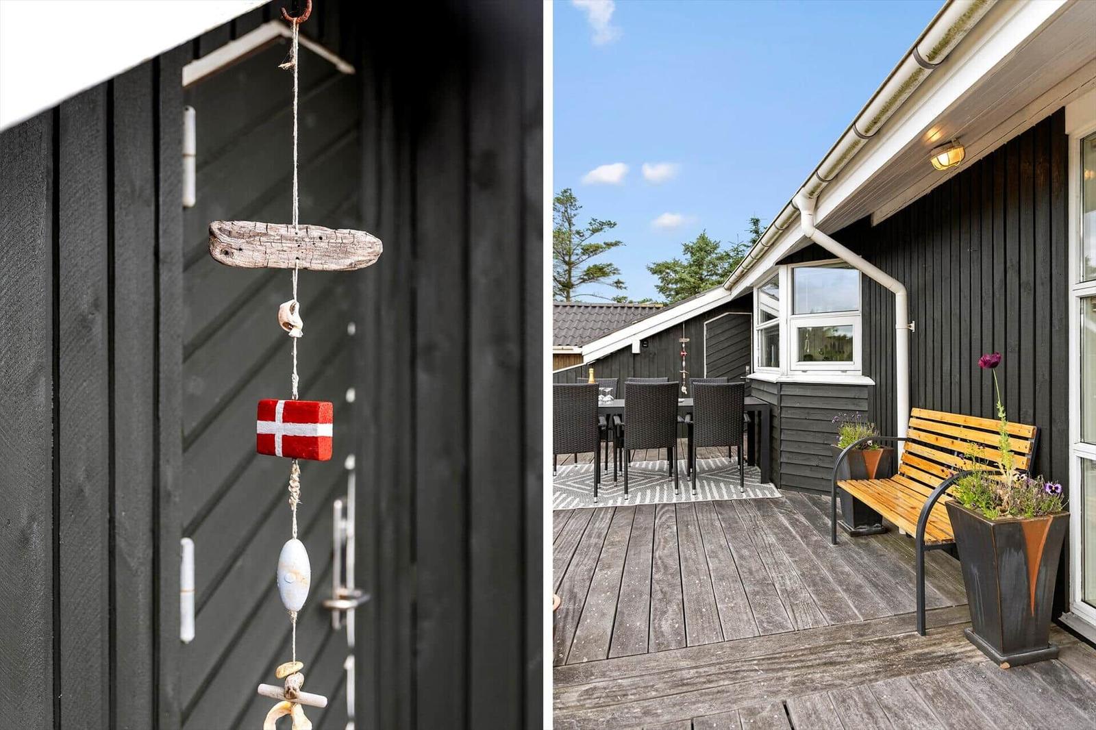 Terrasse mit Holzbank, Tisch und Stühlen. An der Wand hängt ein dekoratives Seil mit dänischer Flagge.