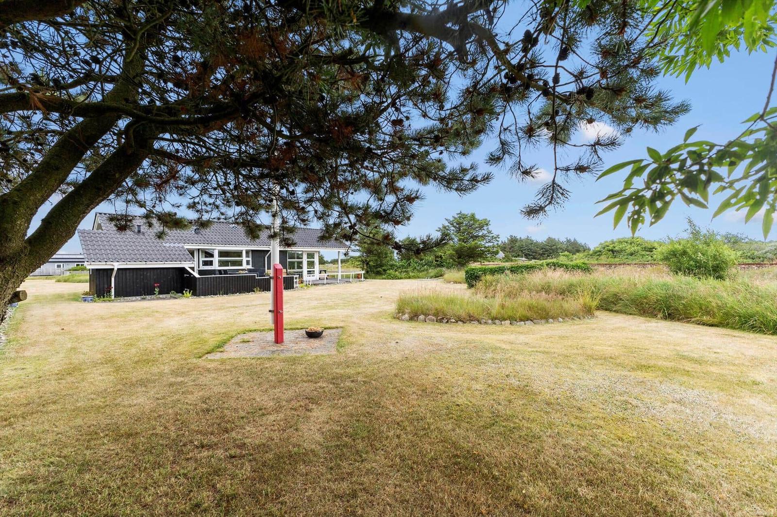 Haus mit Garten unter Bäumen. Roter Pfosten im Vordergrund.