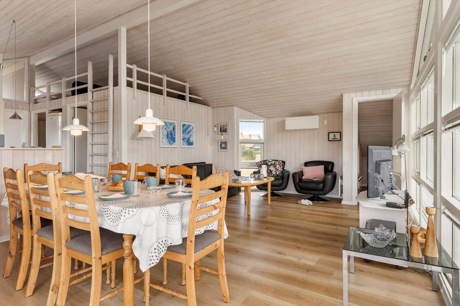 Großes Wohnzimmer mit Essbereich, Holzdecke und -boden, schwarze Sessel und Tisch mit Tischdecke.