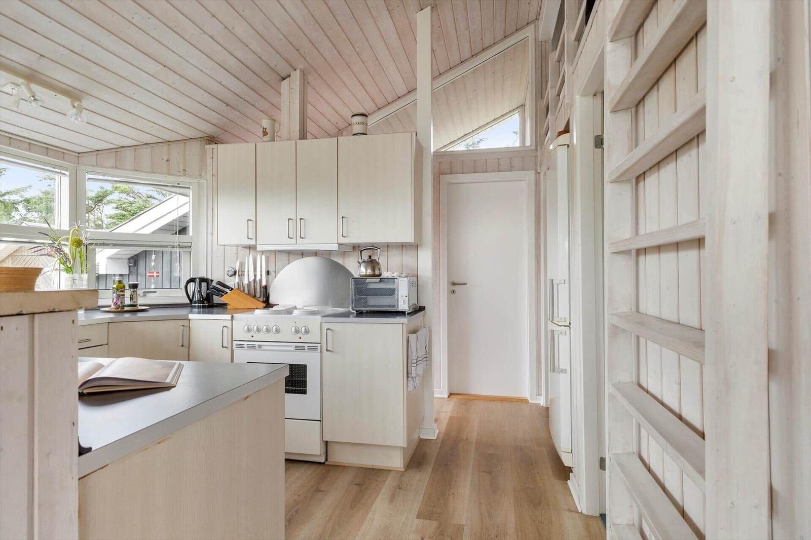 Küche mit Holzdecke, weißen Schränken und Kücheninsel. Fenster, Kühlschrank und Ofen sichtbar.