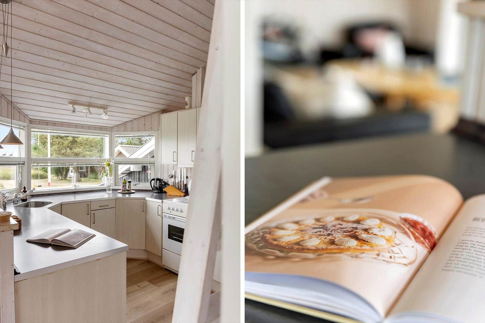 Küche mit Holzdecke und Fenster. Offener Blick auf Wohnzimmer mit Kochbuch.