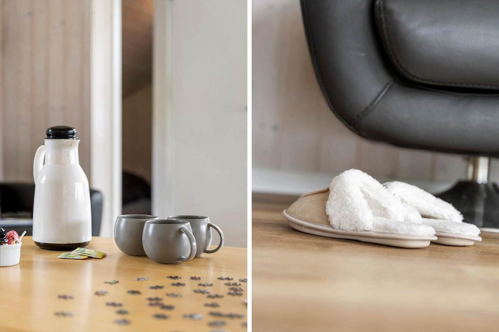 Tisch mit Thermoskanne, Tassen und Puzzleteilen. Weiche Hausschuhe neben einem Sessel.
