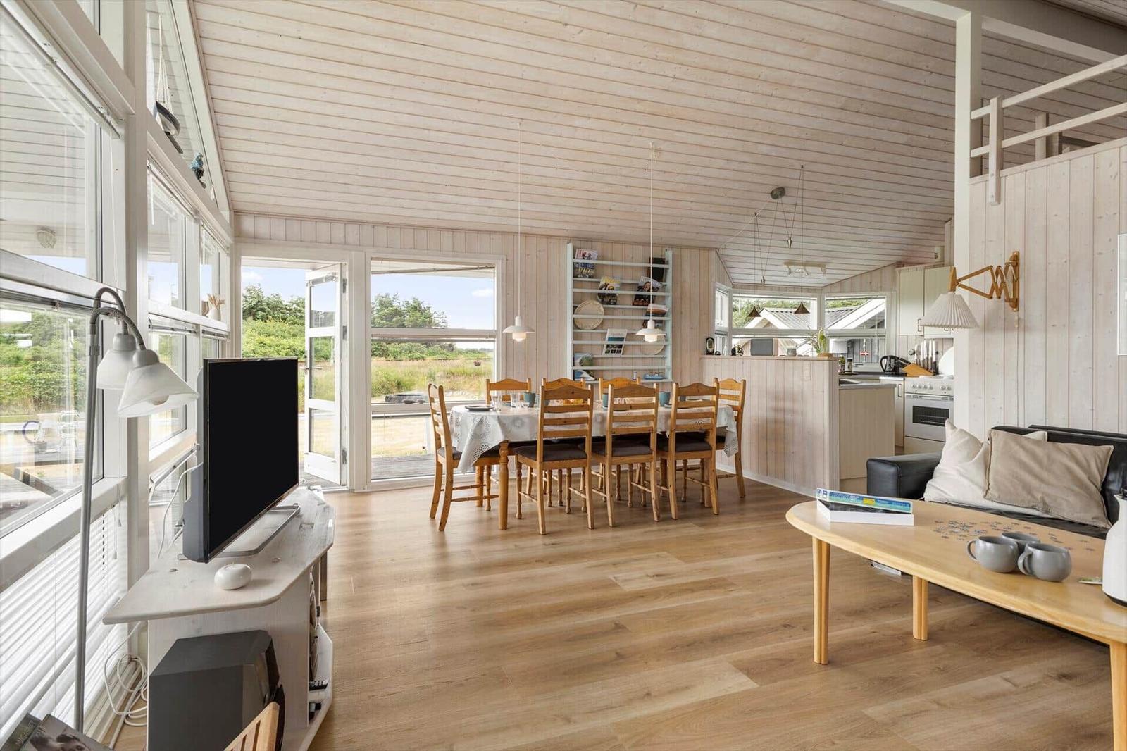 Wohnung mit Essbereich, Küche und Sofa. Holzboden und Decke. Fenster und Türen zur Außenseite.