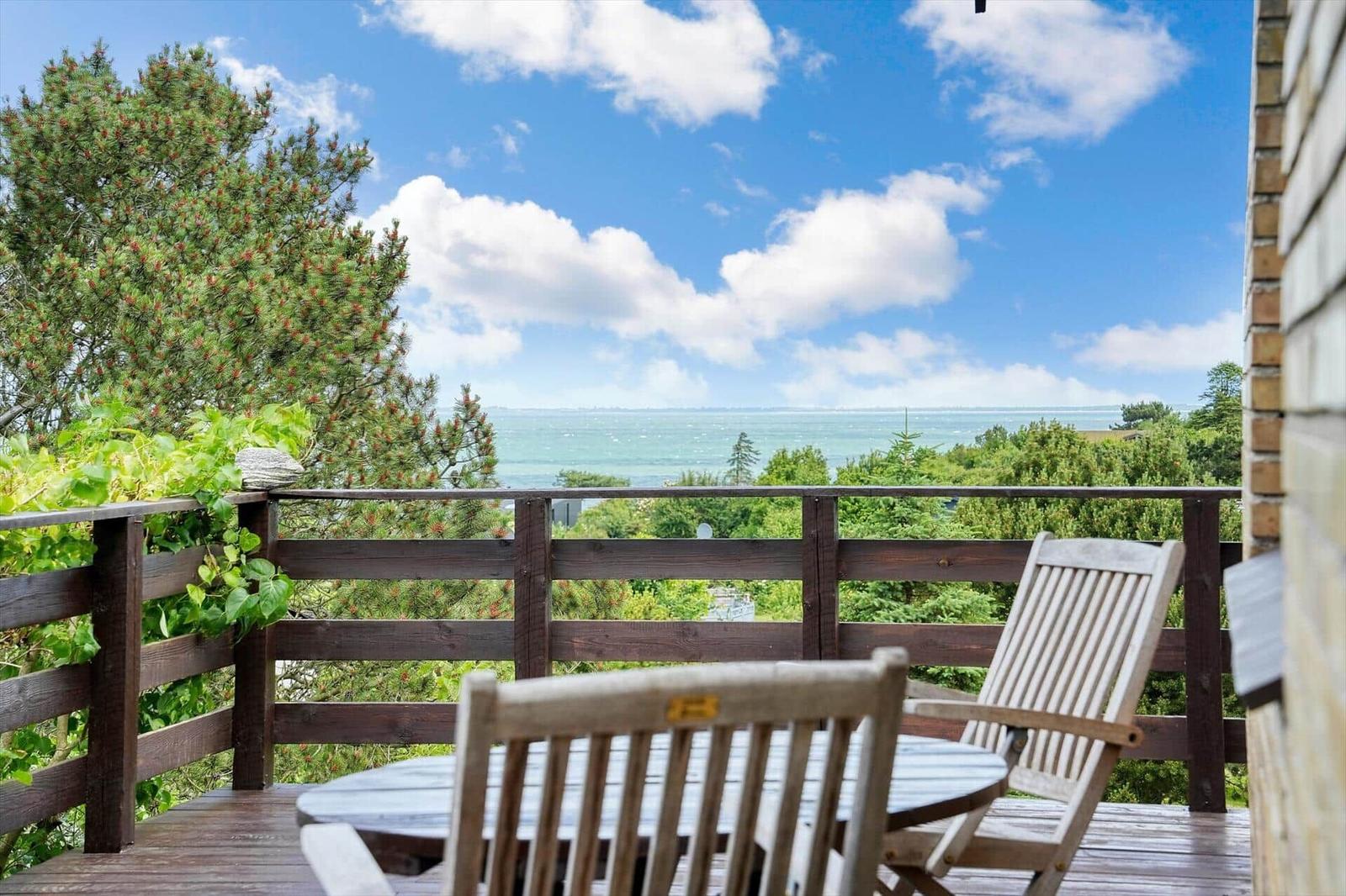 Deck with table and chairs offers ocean view through trees.