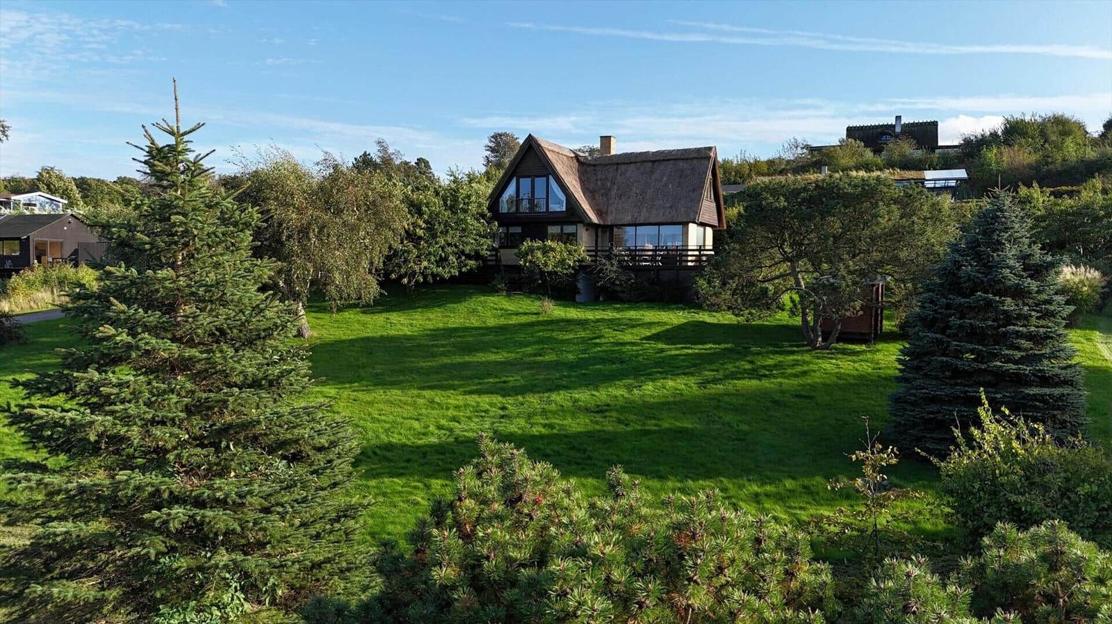 A house with a thatched roof stands on a green lawn surrounded by trees.
