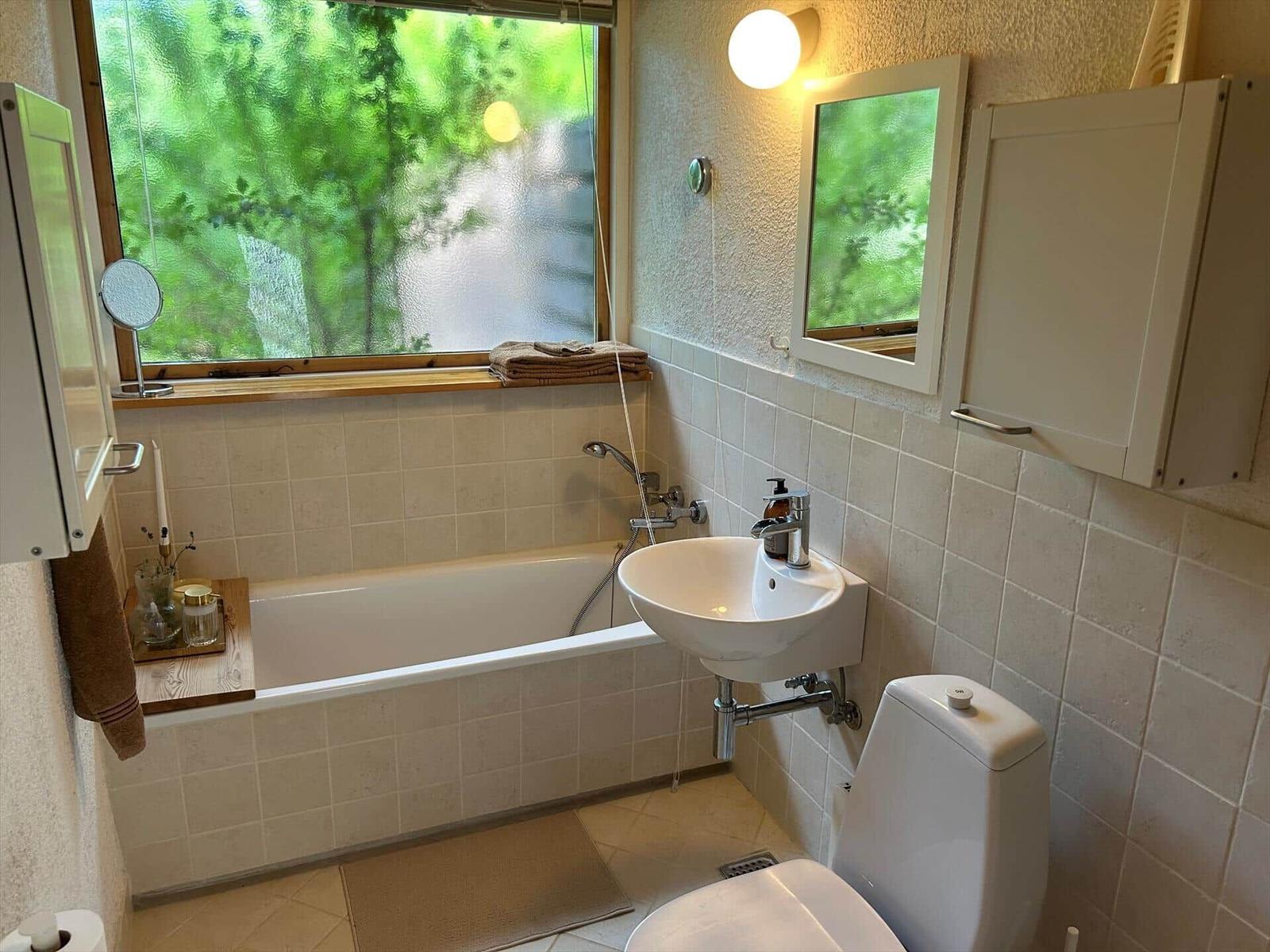 Bathroom with bathtub, sink, and toilet. Window with view of green trees.