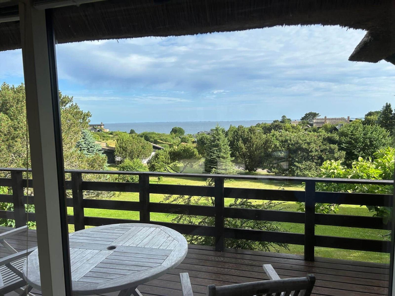 Terrace with table and chairs offers view of green areas and sea.