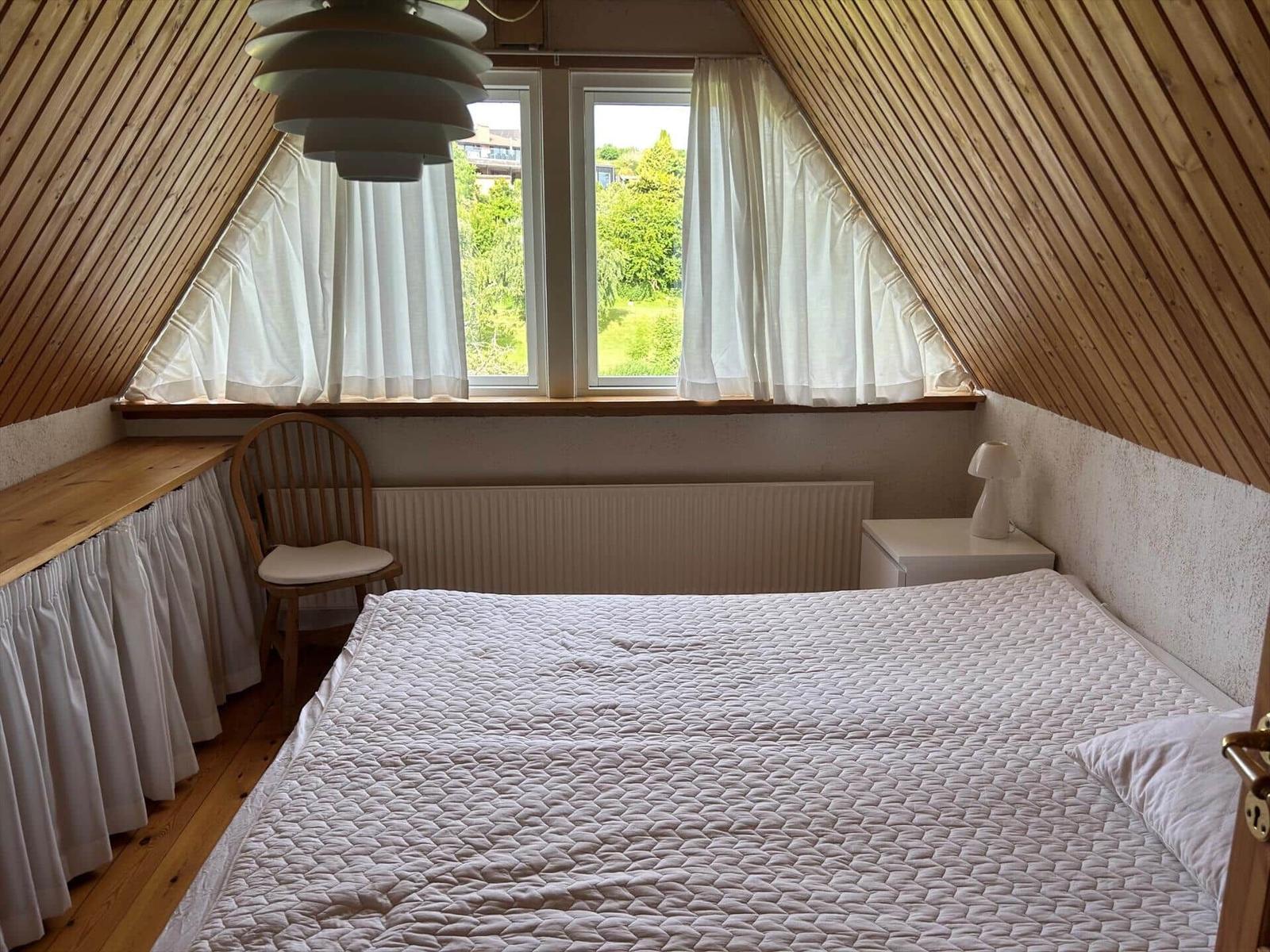 Bedroom with sloped ceiling, window, bed, and desk.