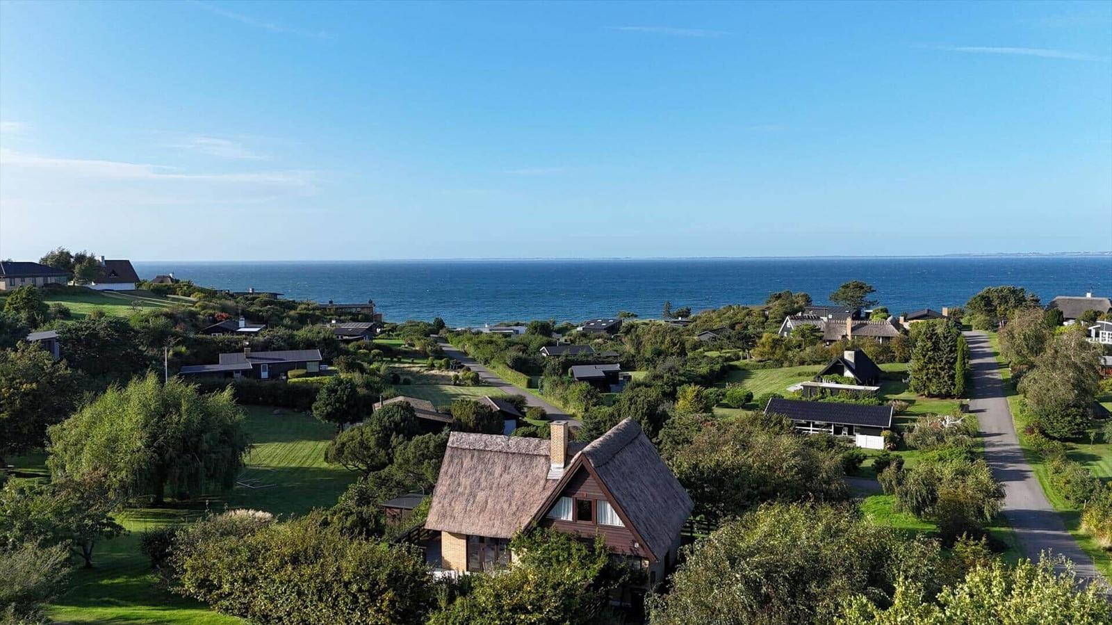 House with thatched roof, surrounded by greenery and trees, view of the sea.