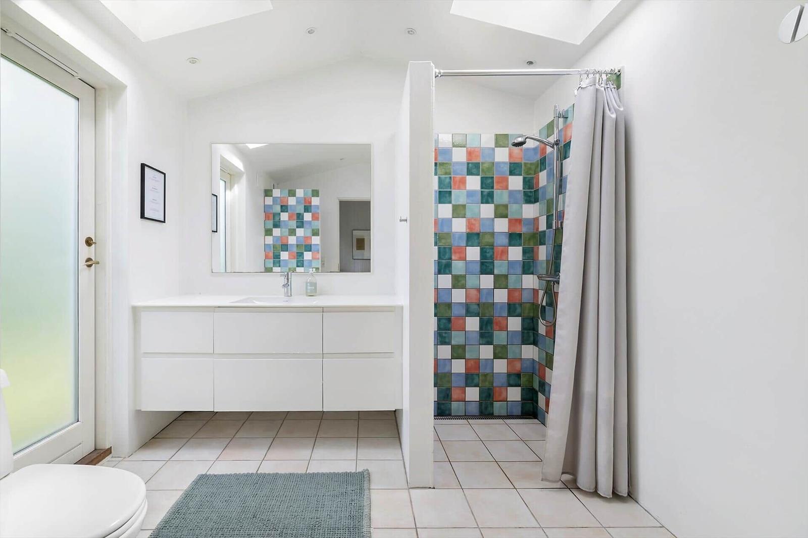 Bathroom with shower, sink and toilet. Walls tiled with colorful squares.