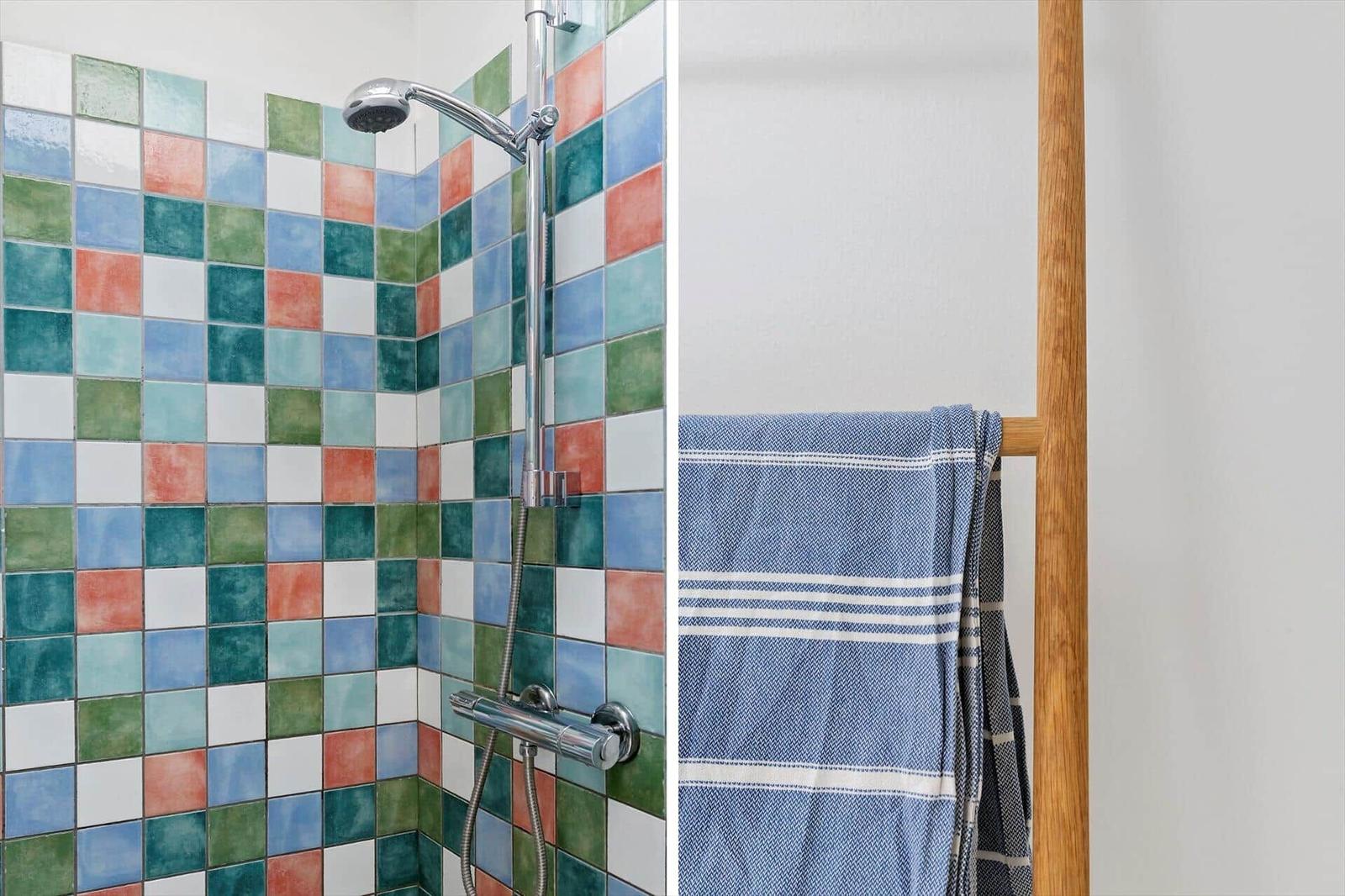 Shower area with colorful tiles and wooden towel rack with blue towel.
