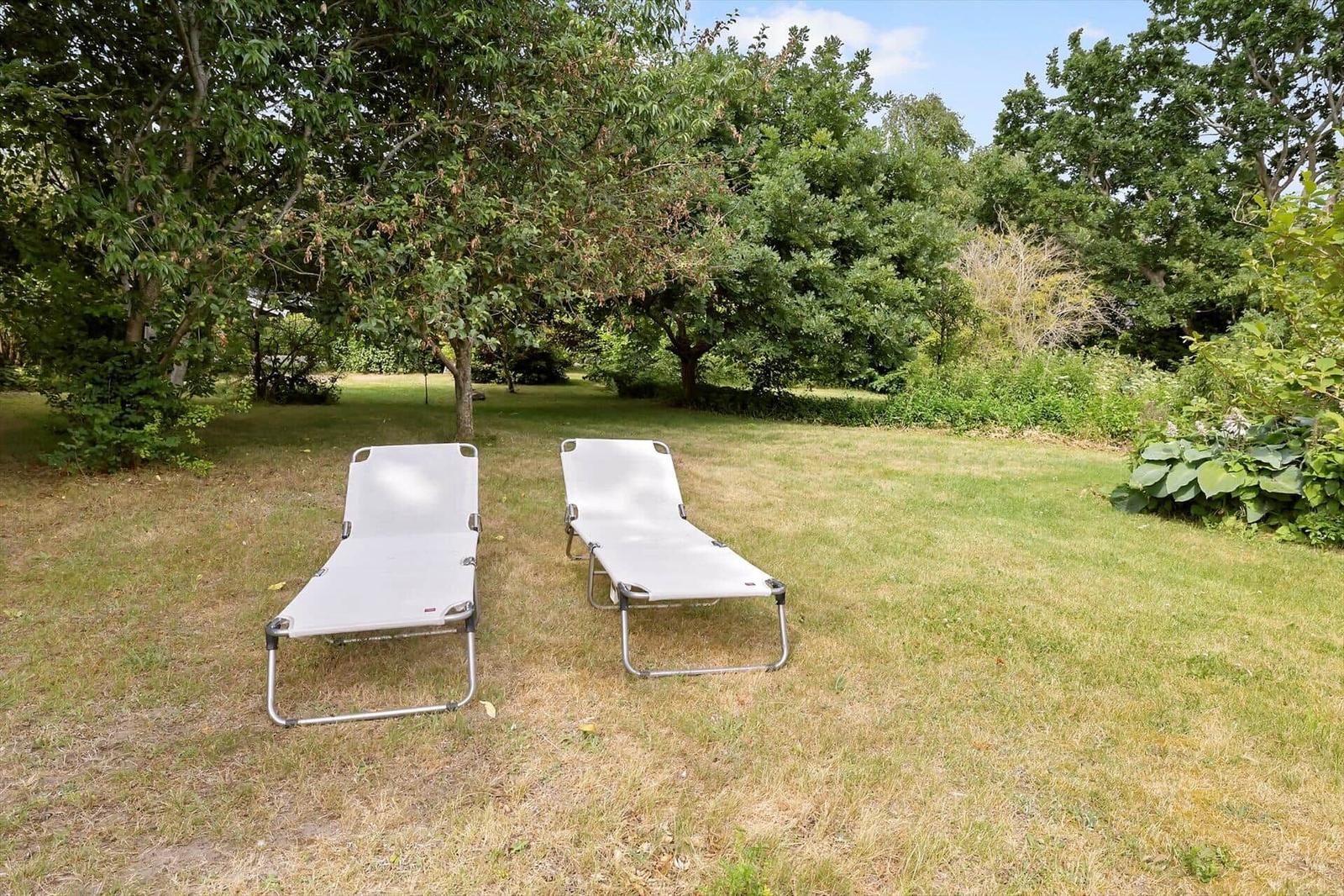 Two white lounge chairs are on a lawn under trees.