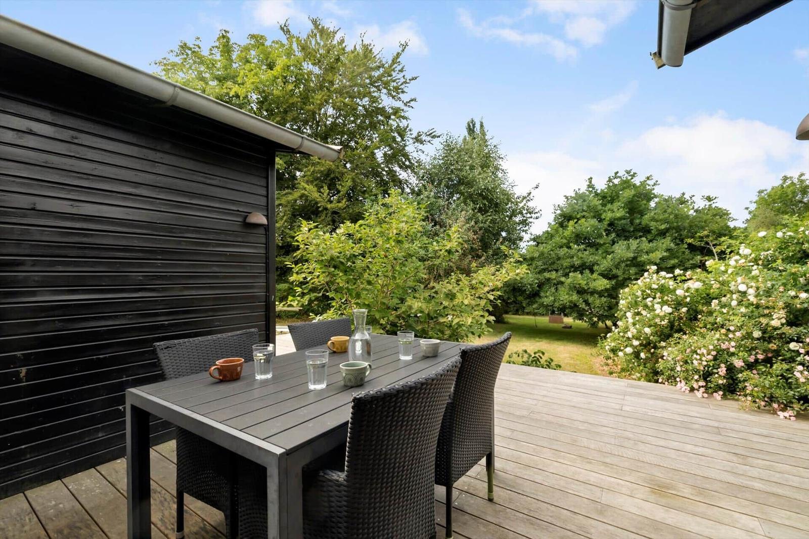 Terrace with table and chairs, view of green garden with flowers.