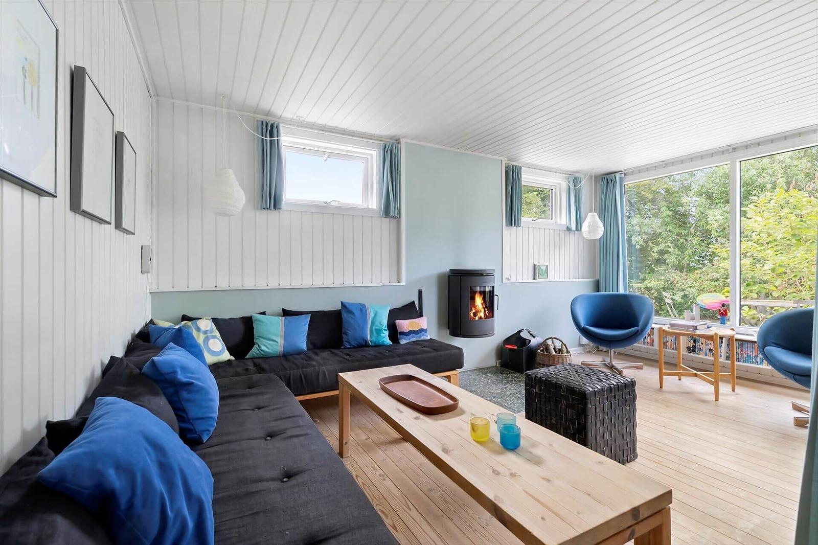Living room with sofa, fireplace, and seating. Wooden floor and large windows.