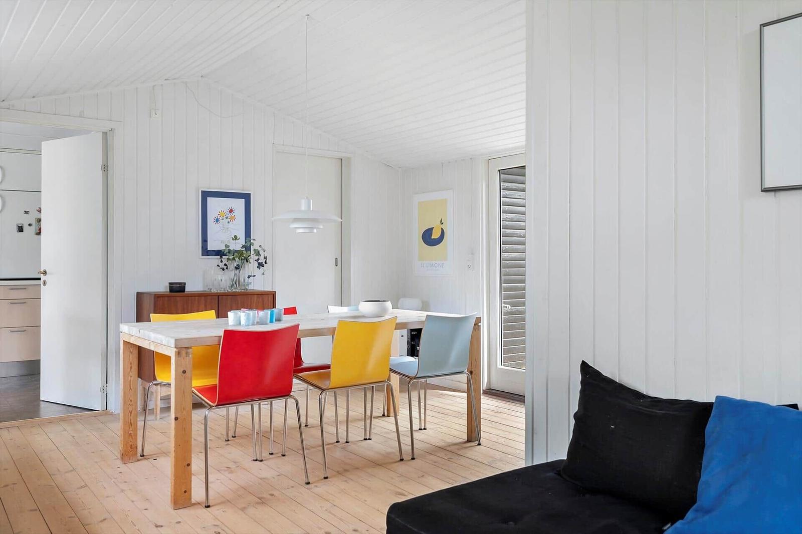 Dining room with colorful chairs and wooden floor. Kitchen and bedroom in the background.