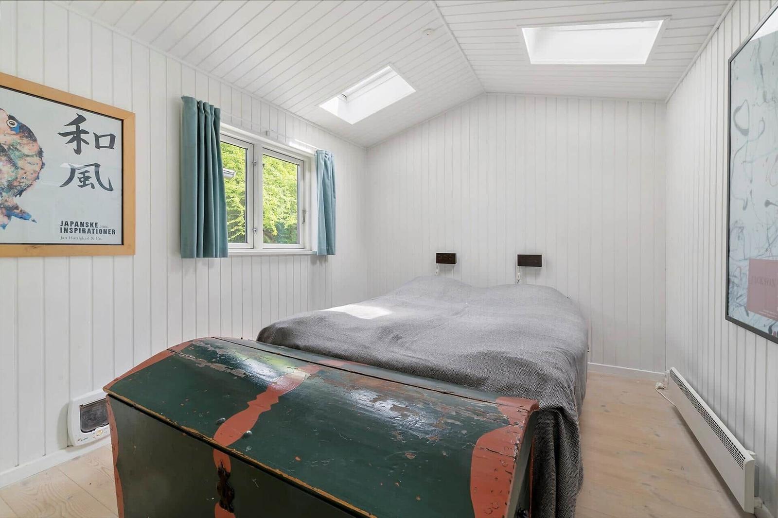 Bedroom with bed, window, skylights, and old trunk.