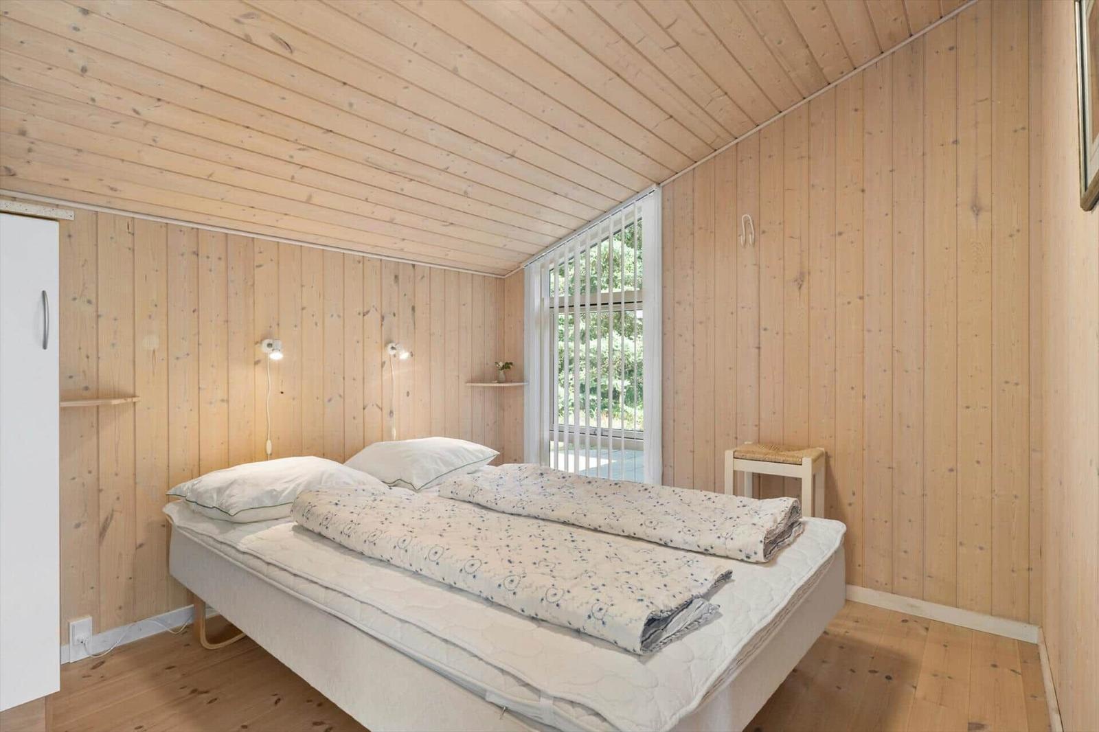 Schlafzimmer mit Holzwandverkleidung, Bett, Fenster und Kleiderschrank.