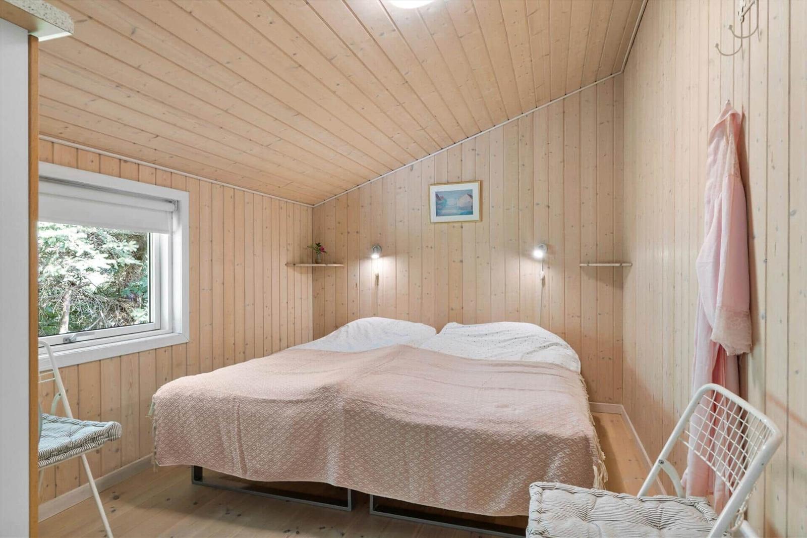 Schlafzimmer mit Holzwand, Bett, Fenster und Stuhl.