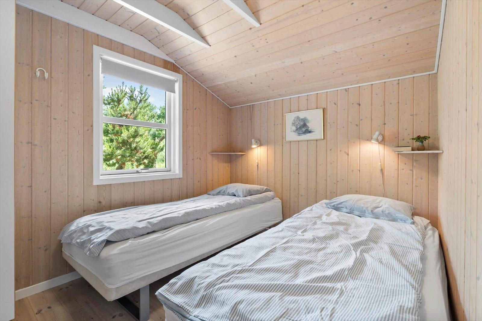 Zwei Einzelbetten in einem Holzraum mit Fenster und Wandlampen.