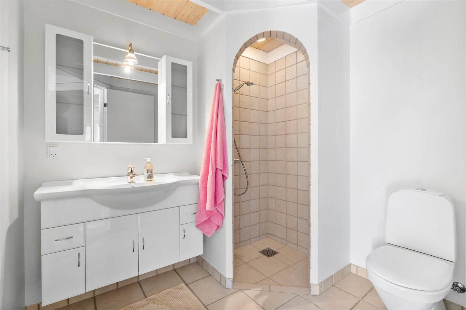 Badezimmer mit Dusche, Waschbecken und Toilette. Ein rosa Handtuch hängt an der Wand.