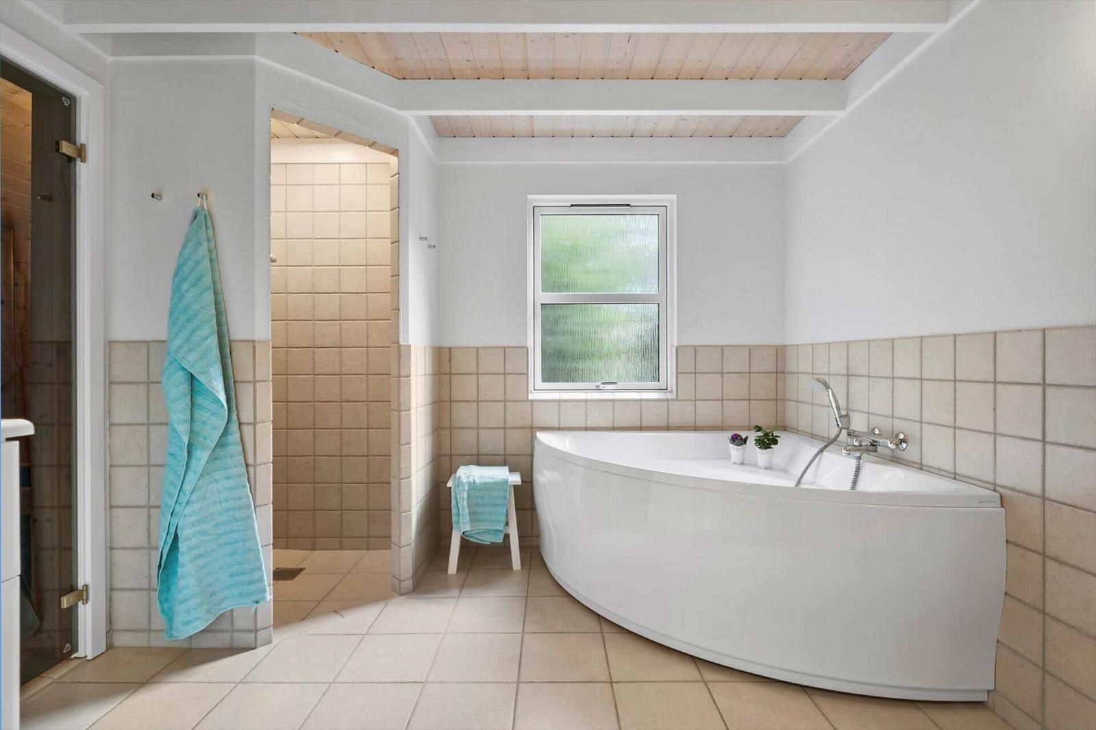 Bad mit freistehender Badewanne, Dusche und Fenster. Holzdecke und Fliesenwand.