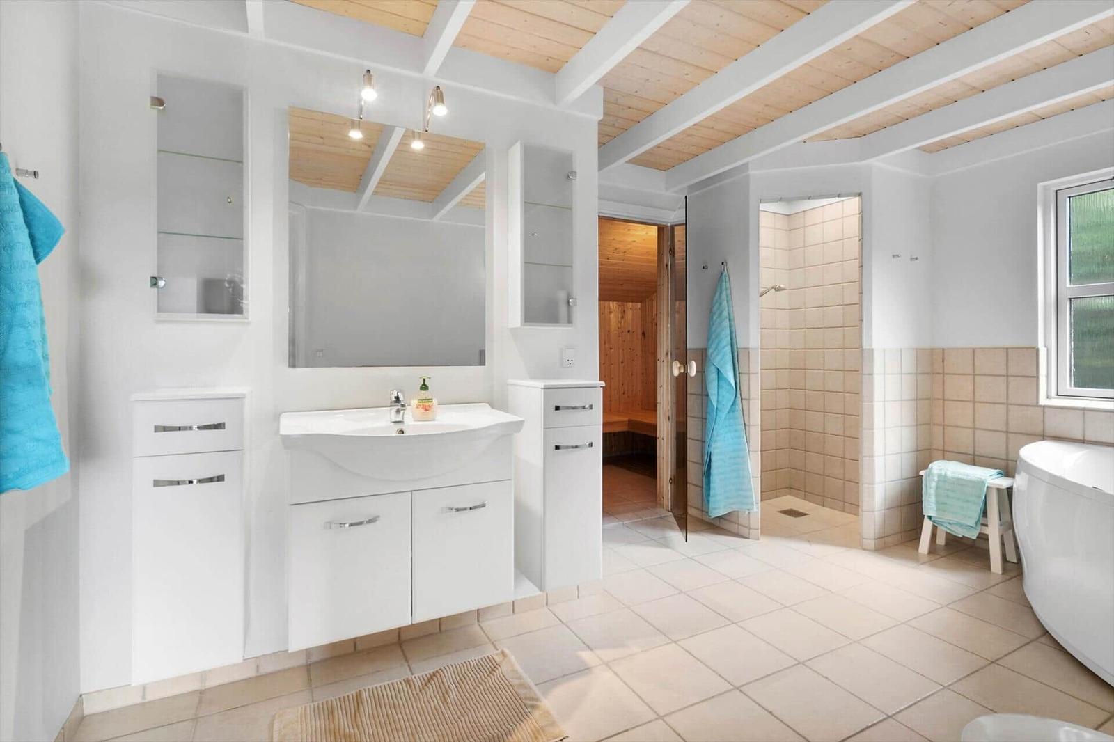 Badezimmer mit Dusche, Badewanne und Sauna. Weiße Einbauschränke und Holzdecke.