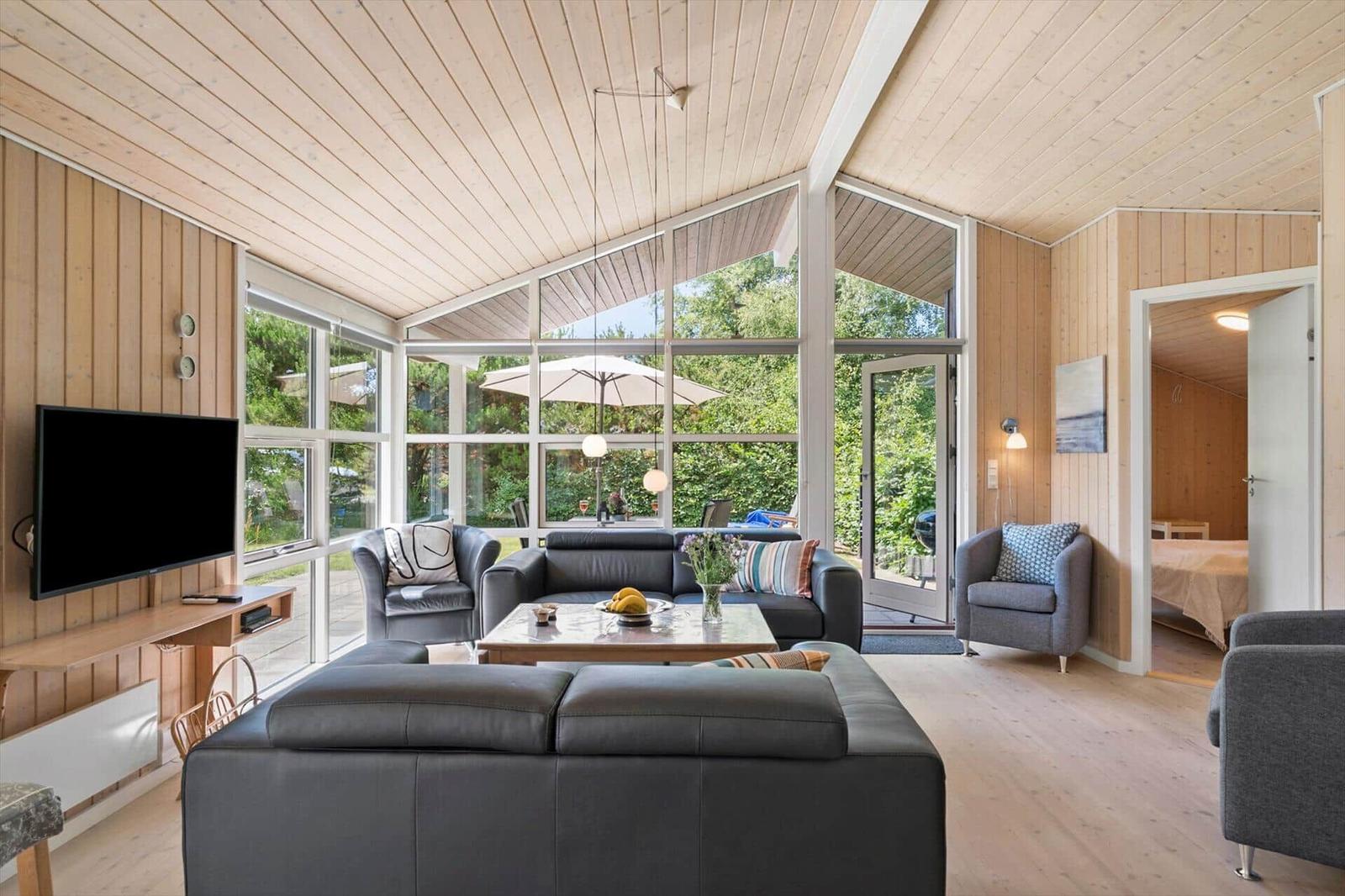 Wohnzimmer mit großem Fenster, Sofa, Fernseher und Blick auf Garten.