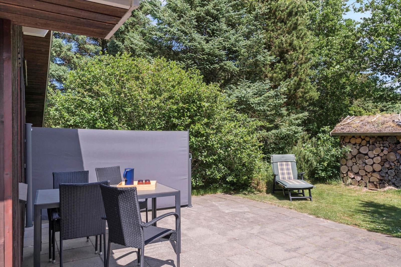 Terrasse mit Tisch, Stühlen und Sonnenschutz. Hinterhof mit Liegestuhl und Holzstapel.