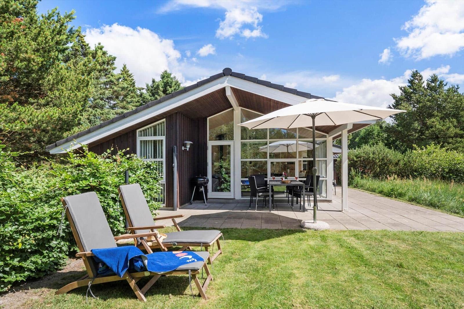 Haus mit Terrasse, Sonnenschirm, Grill und Liegestühle im Garten.