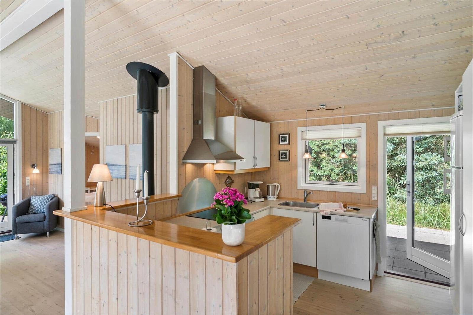 Küche mit Holzvertäfelung, Arbeitsplatte und Fenster zur Außenterrasse.