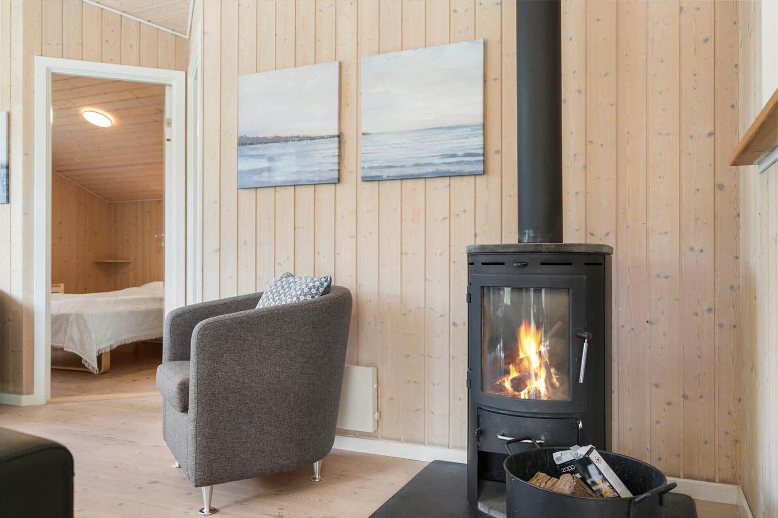 Wohnraum mit Kaminofen, Sessel und Blick in Schlafzimmer.