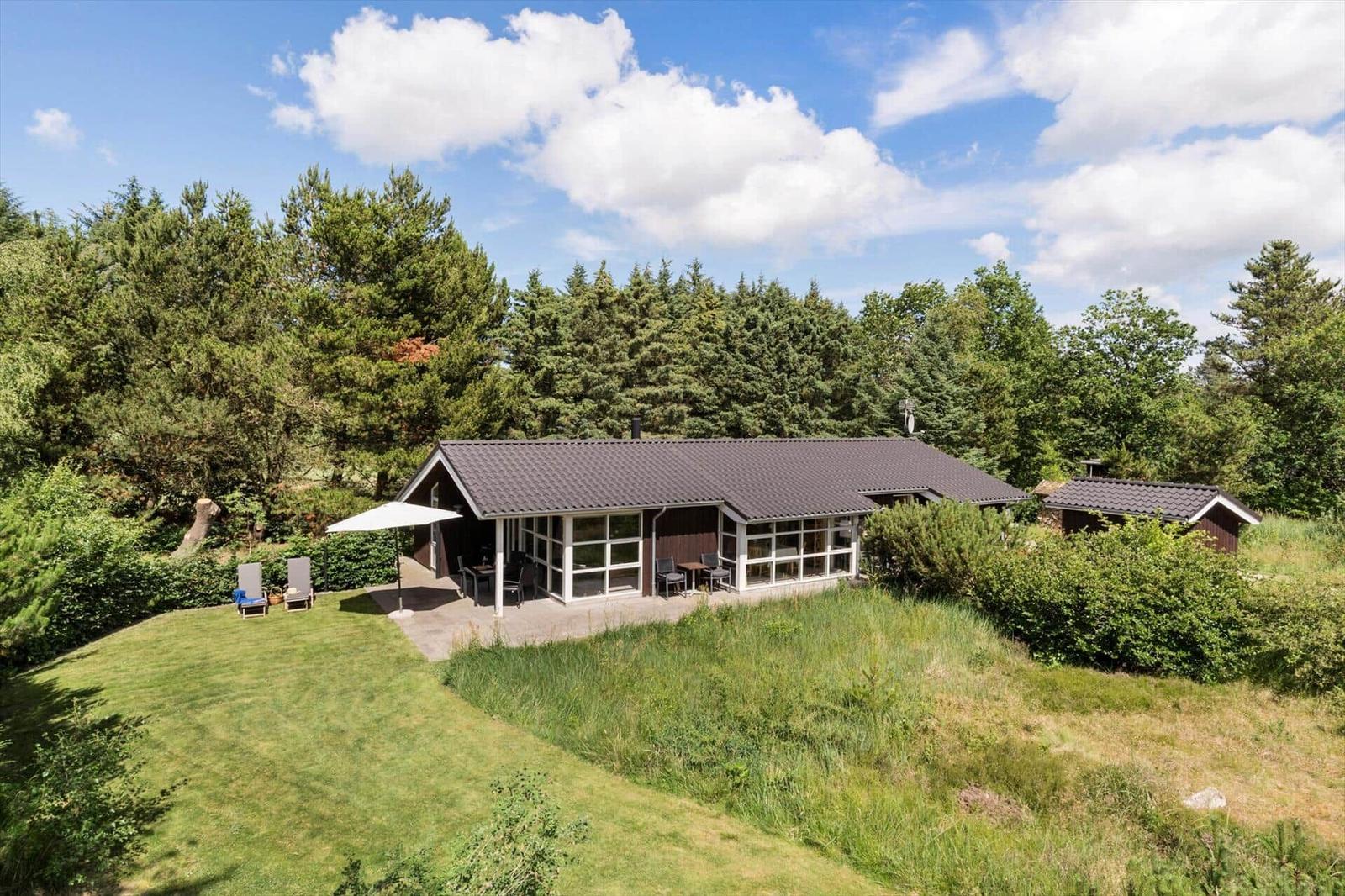 Moderne Ferienhaus mit Terrasse, Garten und Blick auf Wald.