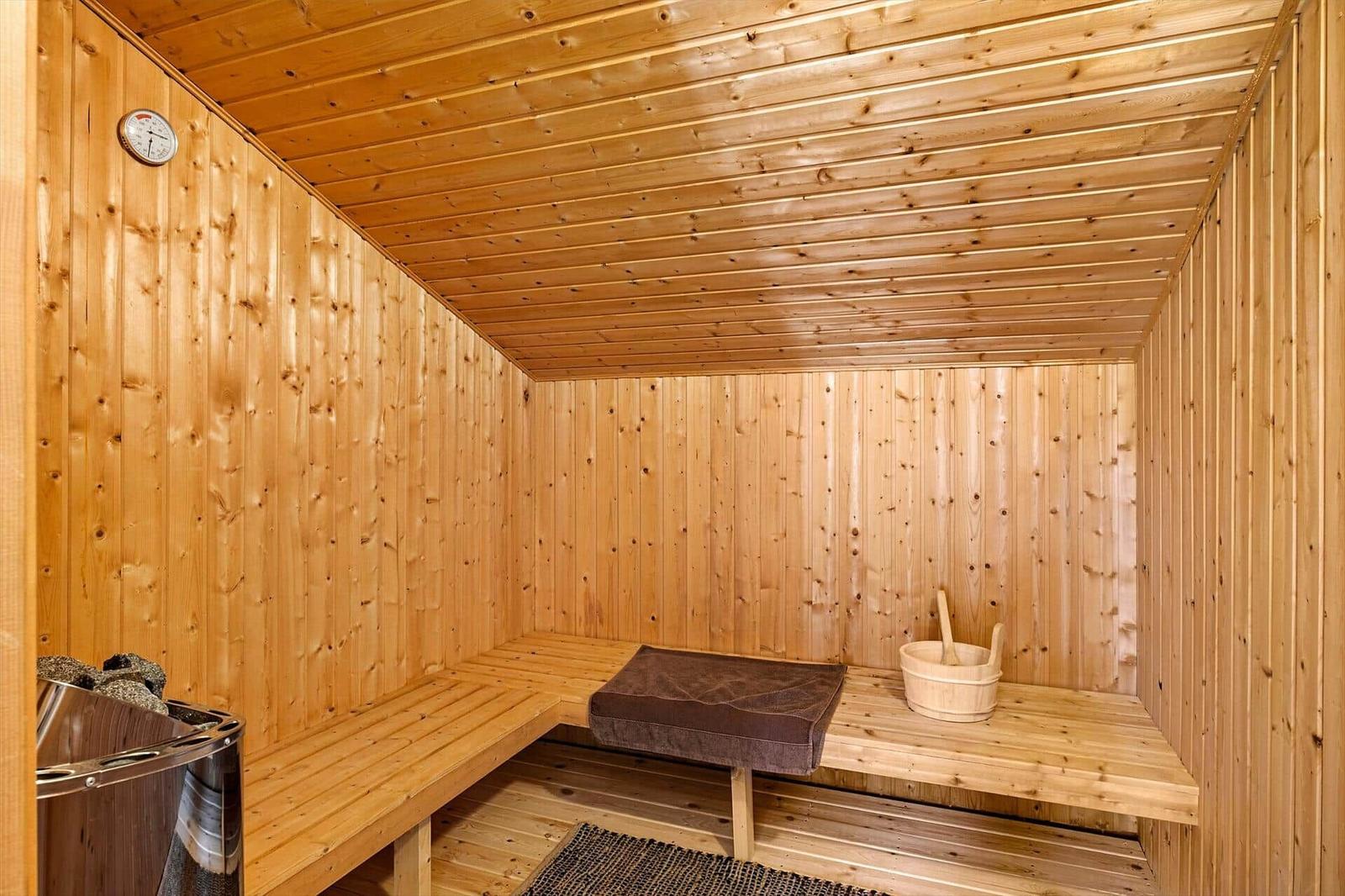 Sauna mit Holzwandverkleidung, Sitzbank und Holzwanne mit Besen.